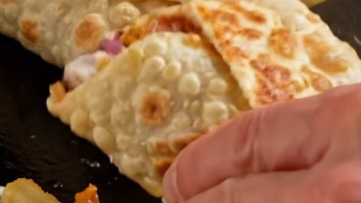 Golden crispy chicken shawarma wrap sliced in half showing layers of chicken, fries, onions, and pickles