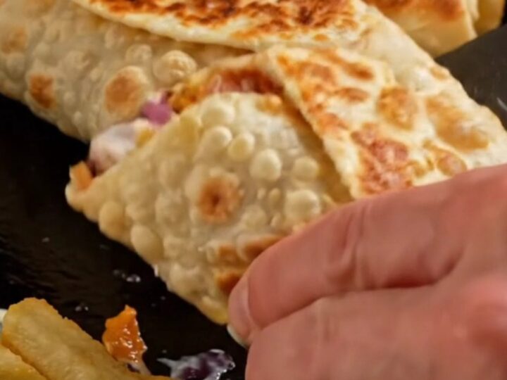 Golden crispy chicken shawarma wrap sliced in half showing layers of chicken, fries, onions, and pickles