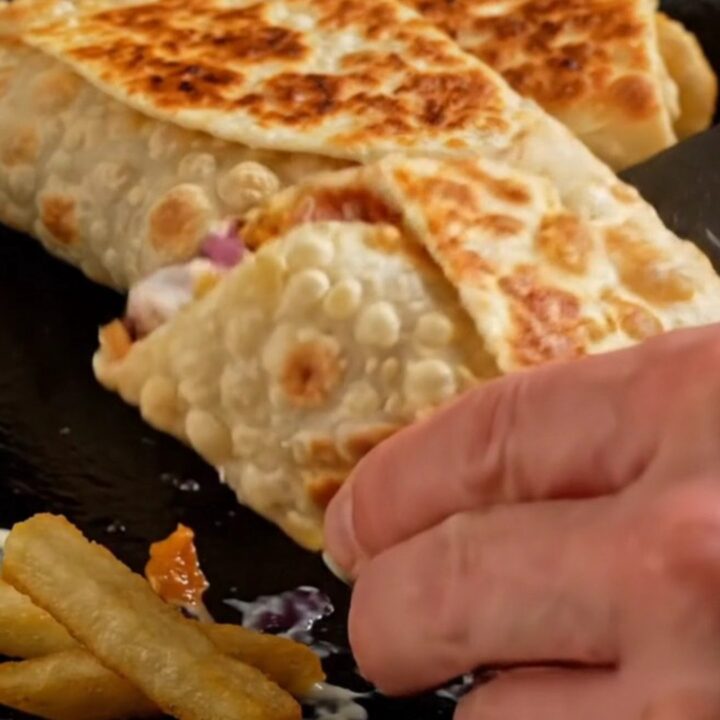 Golden crispy chicken shawarma wrap sliced in half showing layers of chicken, fries, onions, and pickles