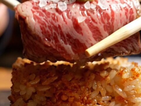 Torched A5 Wagyu on crispy garlic rice with a quail egg yolk, flaky salt, and fresh wasabi, served on a dark plate.