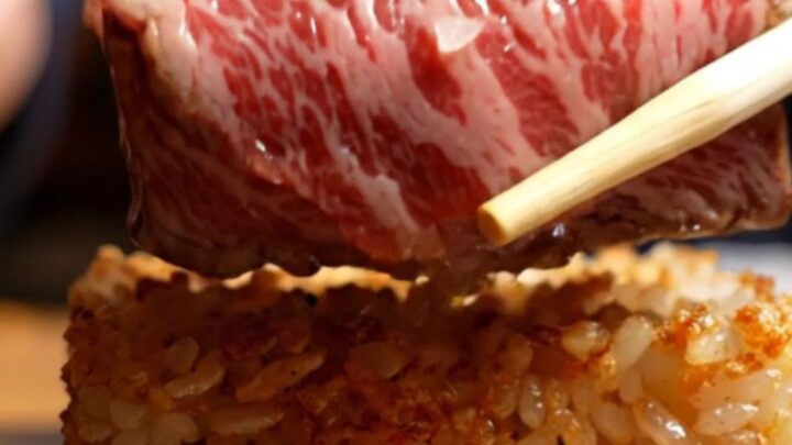 Torched A5 Wagyu on crispy garlic rice with a quail egg yolk, flaky salt, and fresh wasabi, served on a dark plate.