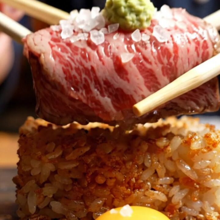 Torched A5 Wagyu on crispy garlic rice with a quail egg yolk, flaky salt, and fresh wasabi, served on a dark plate.