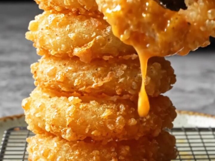 Golden crispy onion rings piled on a plate with a bowl of spicy remoulade sauce.