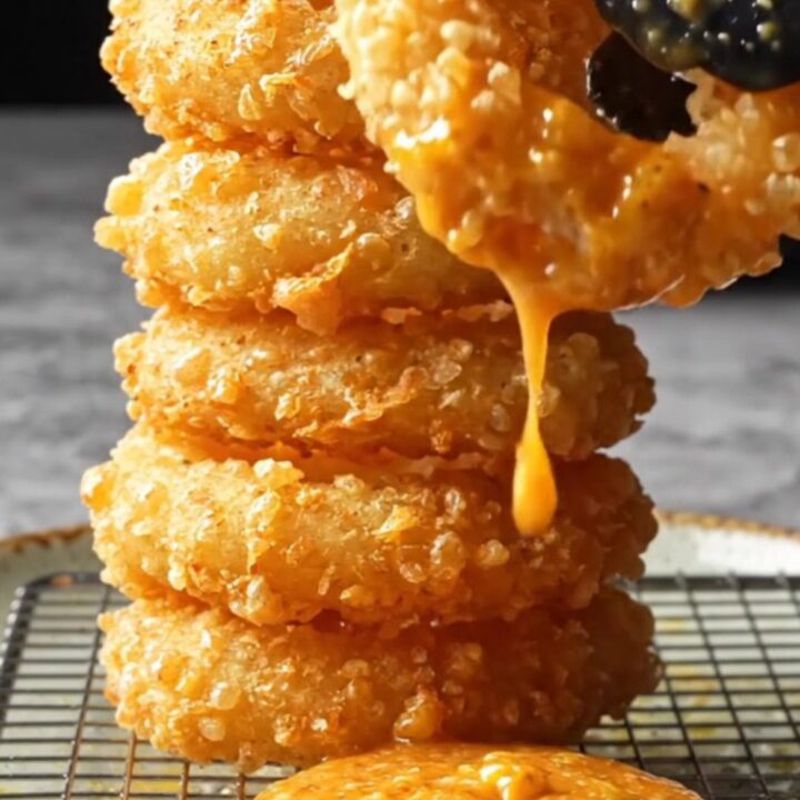 Golden crispy onion rings piled on a plate with a bowl of spicy remoulade sauce.