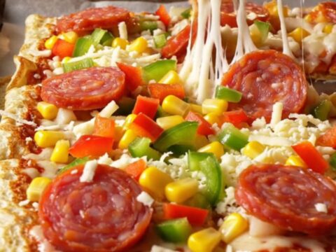 Golden sheet pan crepe pizza squares with melted mozzarella, sucuk, corn, and peppers on a parchment-lined pan.