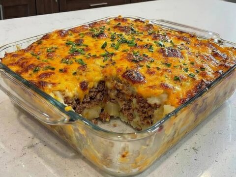 A hearty serving of loaded potato meatloaf casserole in a glass dish with a gooey cheese pull.