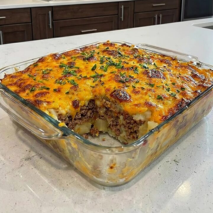 A hearty serving of loaded potato meatloaf casserole in a glass dish with a gooey cheese pull.
