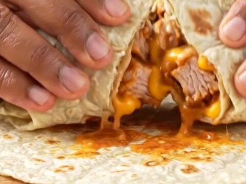 Crispy golden burrito sliced diagonally showing layers of chicken, lettuce, tomatoes, and melted cheese on a plate