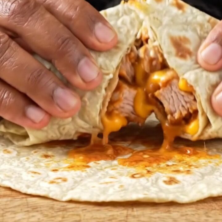 Crispy golden burrito sliced diagonally showing layers of chicken, lettuce, tomatoes, and melted cheese on a plate