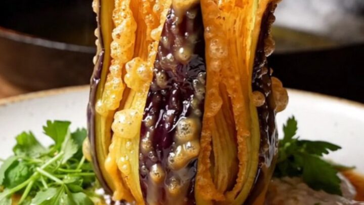 A crispy blooming eggplant fan drizzled with garlic yogurt and sizzling pepper butter, served on a white plate.