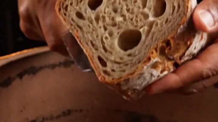 Crusty artisan sourdough loaf with deep mahogany crust and open crumb on a wooden board