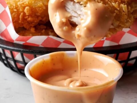 Golden crispy chicken nuggets piled on a plate with a creamy dipping sauce.