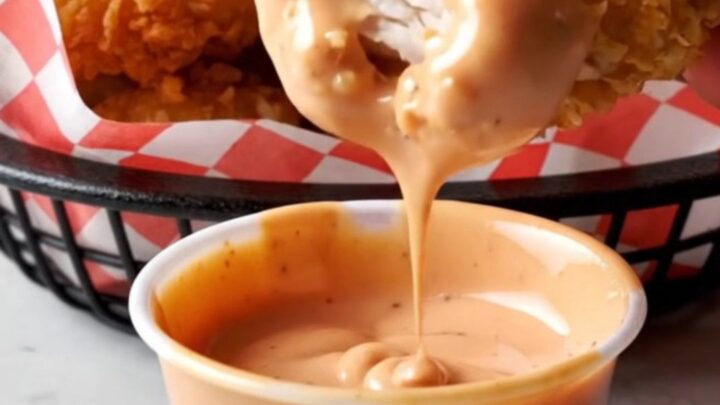 Golden crispy chicken nuggets piled on a plate with a creamy dipping sauce.