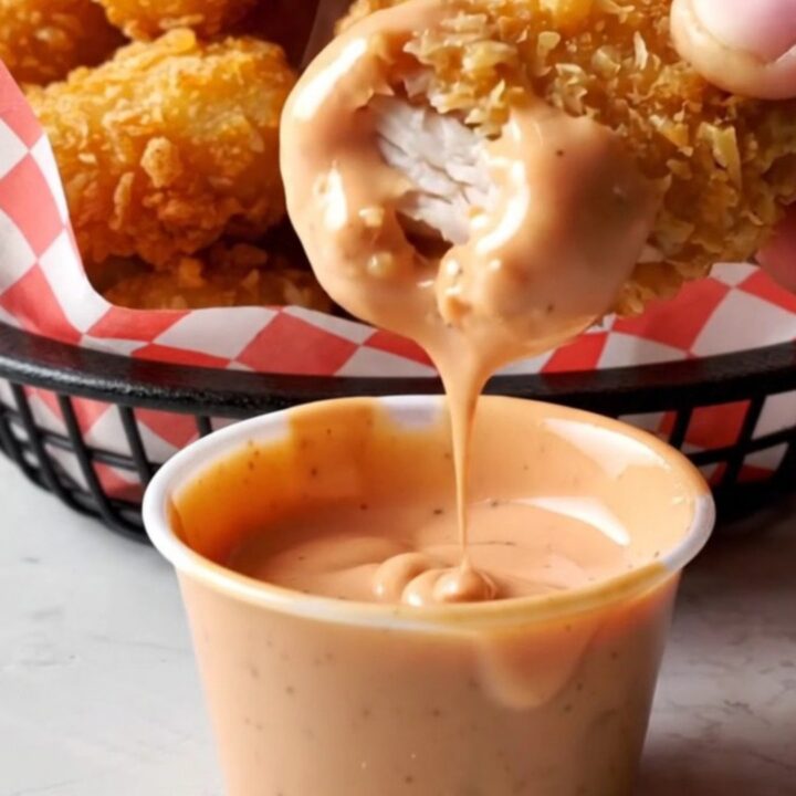 Golden crispy chicken nuggets piled on a plate with a creamy dipping sauce.