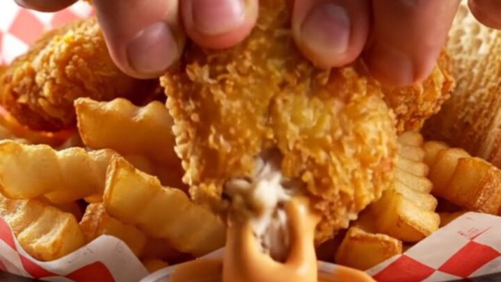 Crispy chicken nuggets piled in a basket with fries and Texas toast, with a cup of creamy pepper sauce for dipping.