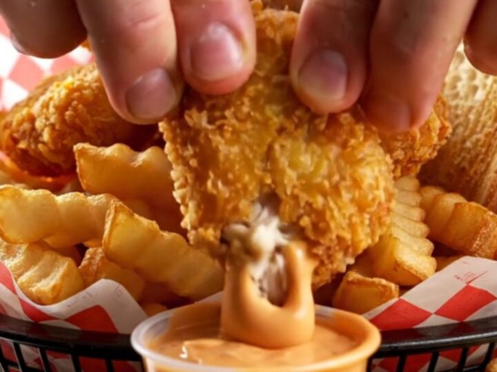 Crispy chicken nuggets piled in a basket with fries and Texas toast, with a cup of creamy pepper sauce for dipping.