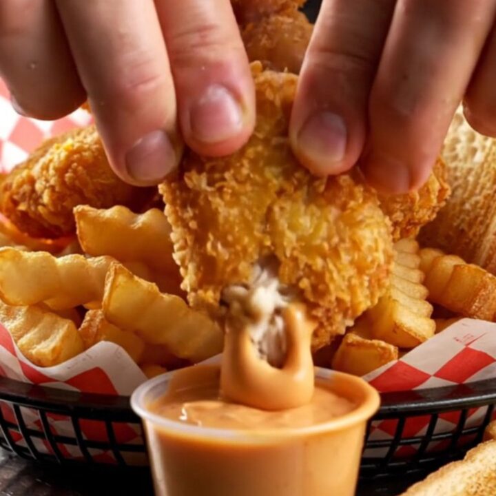Crispy chicken nuggets piled in a basket with fries and Texas toast, with a cup of creamy pepper sauce for dipping.