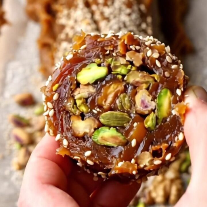 Sliced no-bake cardamom date nut rolls on a wooden board, showing pistachio and walnut mosaic
