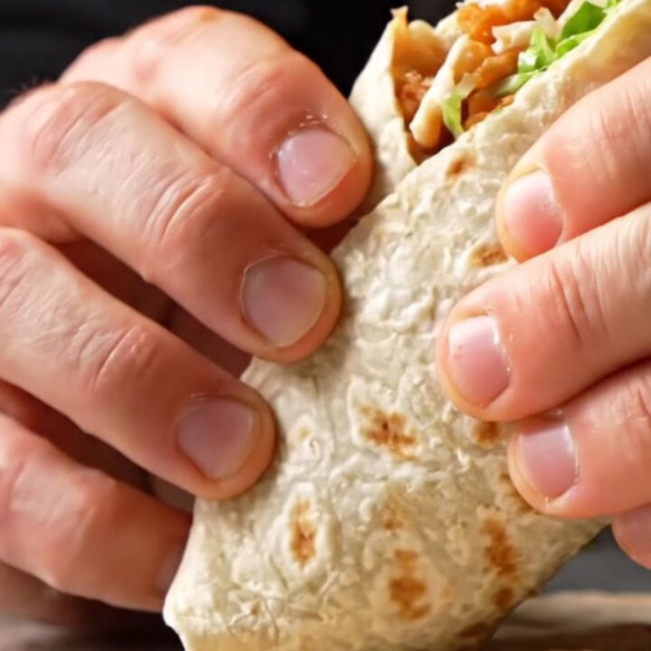 Crispy chicken Caesar wrap sliced diagonally, showing layers of golden chicken, lettuce, and creamy dressing
