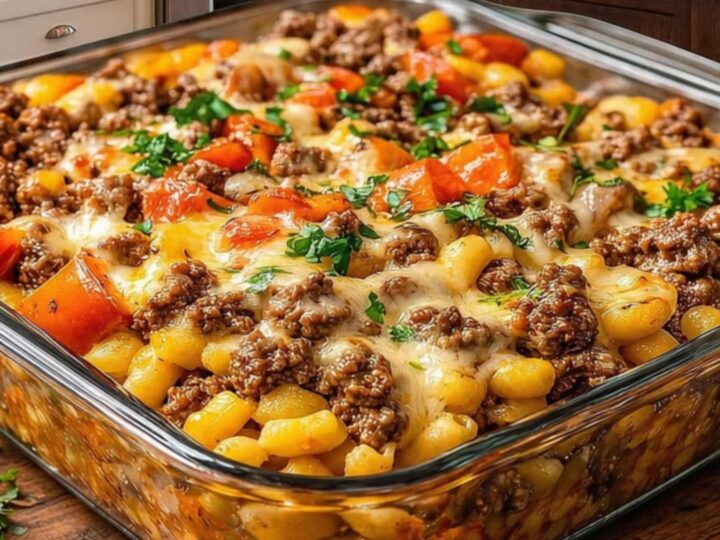 A close-up of a serving spoon scooping out a portion of Hamburger Supreme Casserole with a dramatic melted cheese pull.