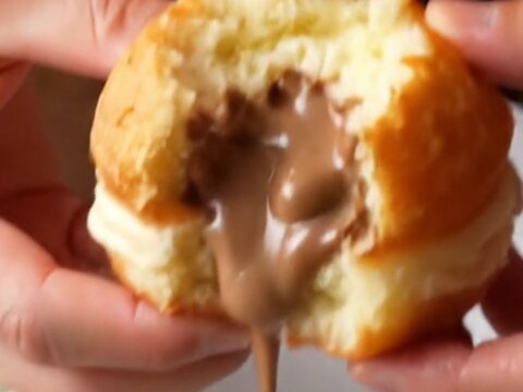 Golden Berliner donuts coated in powdered sugar, one with hazelnut cream oozing out