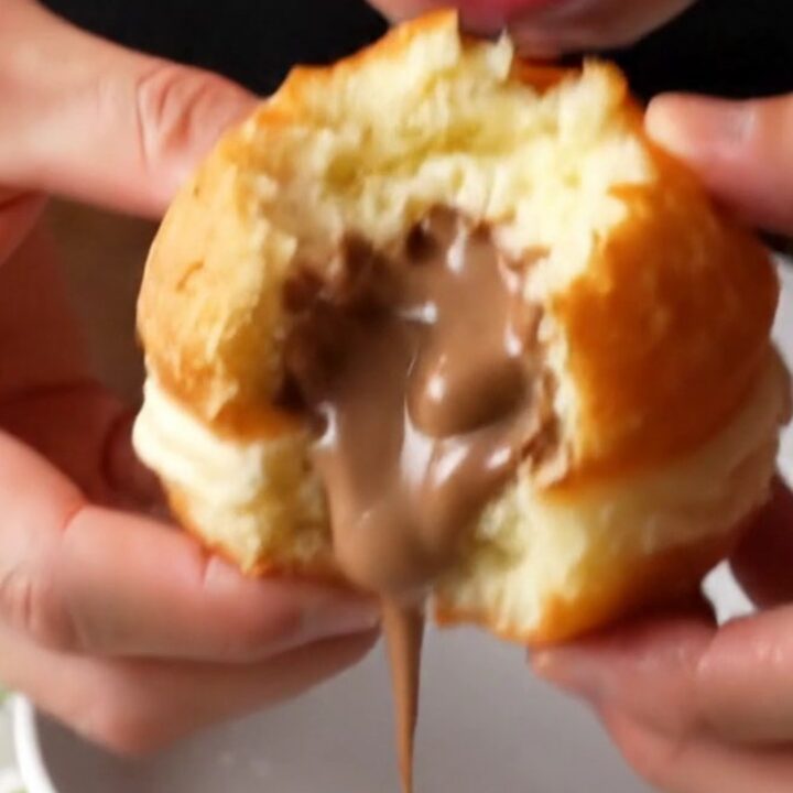 Golden Berliner donuts coated in powdered sugar, one with hazelnut cream oozing out