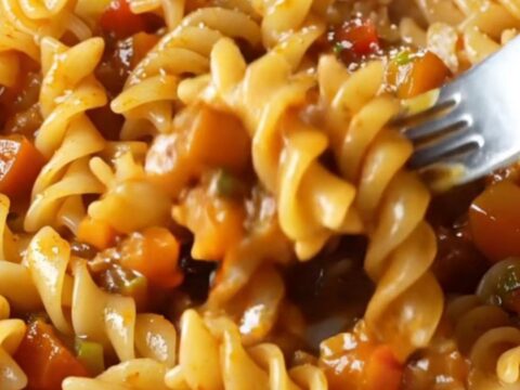 A plate of fusilli pasta coated in a chunky tomato-vegetable ragù with melted mozzarella