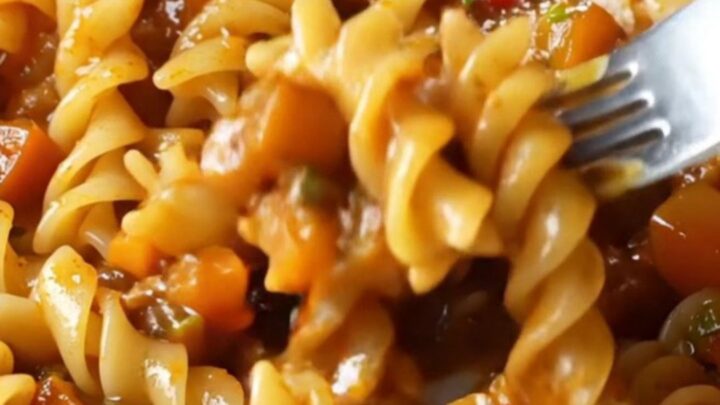 A plate of fusilli pasta coated in a chunky tomato-vegetable ragù with melted mozzarella