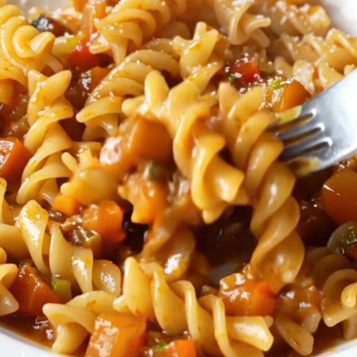 A plate of fusilli pasta coated in a chunky tomato-vegetable ragù with melted mozzarella