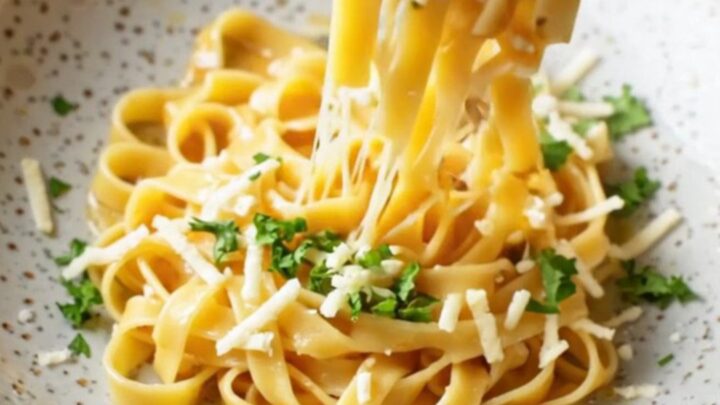 Twirled tagliatelle in a wide ceramic bowl, coated in roasted vegetable sauce with melted mozzarella and Parmesan