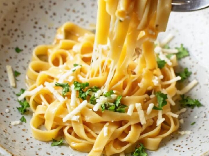 Twirled tagliatelle in a wide ceramic bowl, coated in roasted vegetable sauce with melted mozzarella and Parmesan