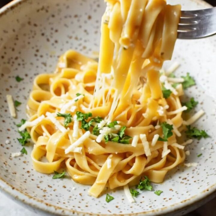Twirled tagliatelle in a wide ceramic bowl, coated in roasted vegetable sauce with melted mozzarella and Parmesan