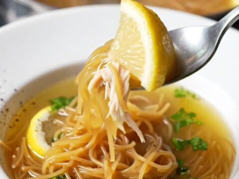 A bowl of golden vermicelli chicken soup with shredded chicken, parsley, and steam rising