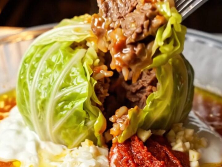 A roasted cabbage parcel sliced open on a bed of cold garlic yogurt, showing the spiced beef and rice filling.