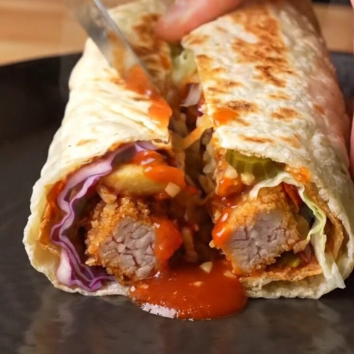 Crispy chicken lavaş wrap sliced in half showing layers of chicken, fries, cabbage, and sauce