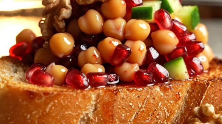 Diced cucumbers, chickpeas, and tomato salad with pomegranate dressing in a glass bowl, garnished with parsley and walnuts.