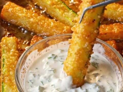 Golden crispy baked zucchini fries with a garlic dill yogurt dip in a small bowl