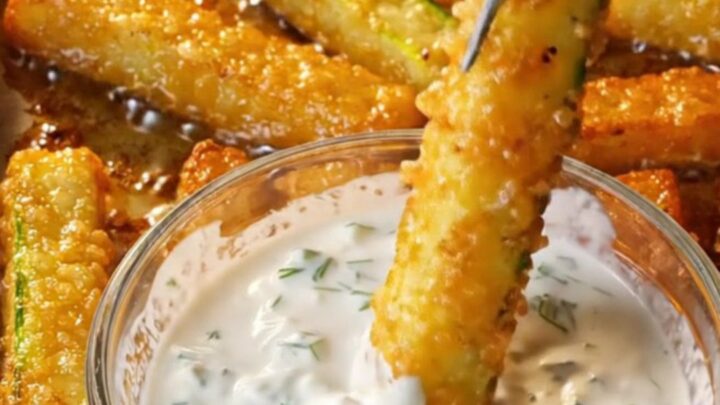 Golden crispy baked zucchini fries with a garlic dill yogurt dip in a small bowl