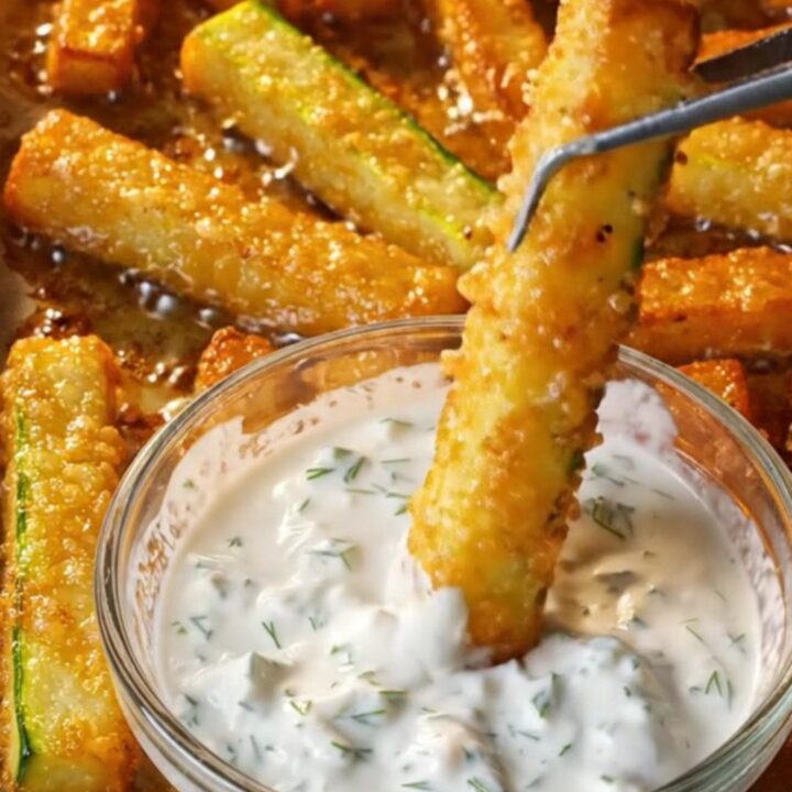Golden crispy baked zucchini fries with a garlic dill yogurt dip in a small bowl