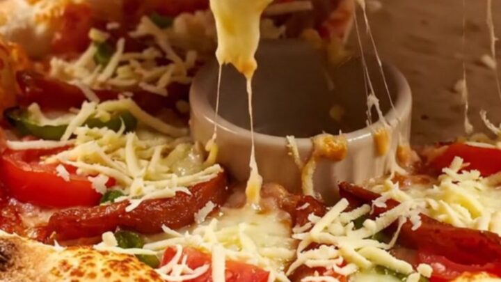 Golden crown ring pizza with melted kaşar cheese, sucuk, tomatoes, and peppers on a parchment-lined baking sheet.