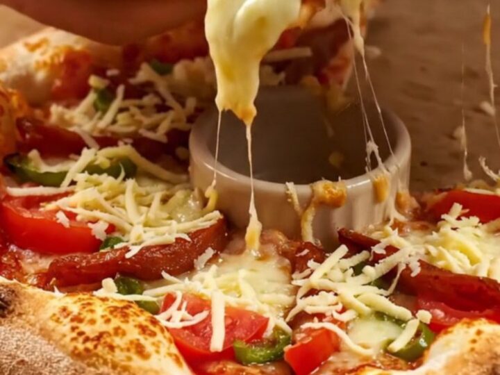 Golden crown ring pizza with melted kaşar cheese, sucuk, tomatoes, and peppers on a parchment-lined baking sheet.