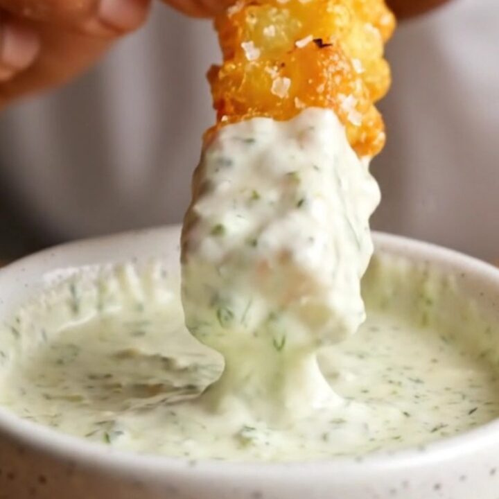 Golden accordion zucchini fries with parmesan coating, served with a bowl of herb yogurt dip.