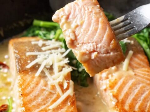 Golden-seared salmon fillets in a creamy parmesan sauce with sun-dried tomatoes and spinach in a skillet