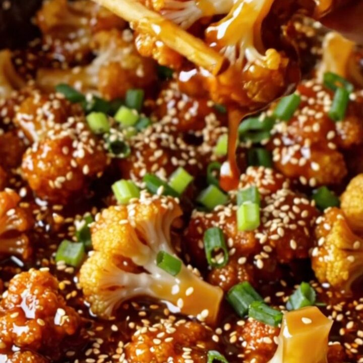 A bowl of crispy air-fried cauliflower bites coated in glossy sesame glaze, topped with sesame seeds and scallions.