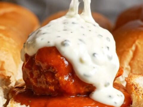 Giant buffalo chicken meatball slider pulled apart with melted mozzarella stretching between the rolls