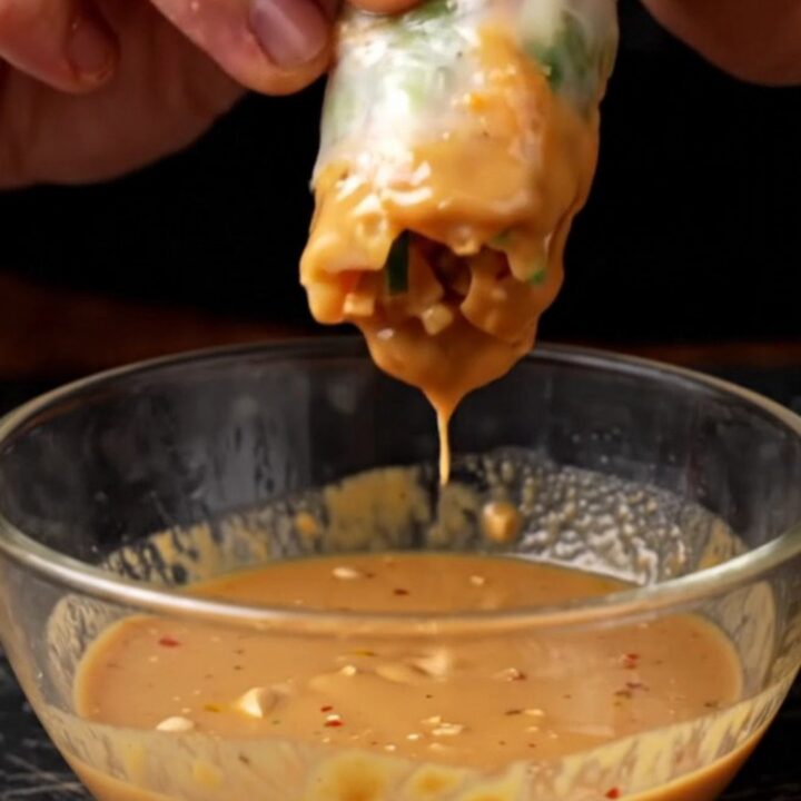 Fresh rice paper spring rolls sliced in half, showing shrimp and purple cabbage, with a bowl of peanut dip