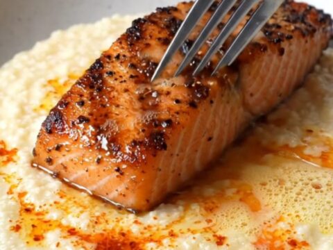 Blackened salmon fillet with charred crust over creamy white cheddar grits, drizzled with spiced butter and chives