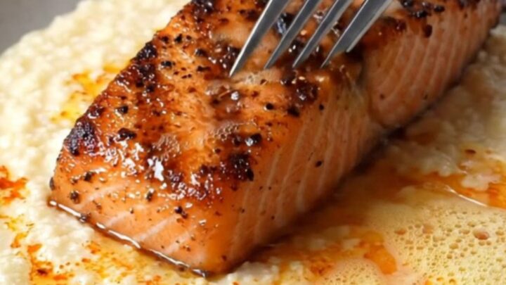 Blackened salmon fillet with charred crust over creamy white cheddar grits, drizzled with spiced butter and chives
