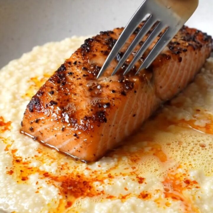 Blackened salmon fillet with charred crust over creamy white cheddar grits, drizzled with spiced butter and chives