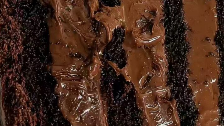 A slice of decadent chocolate fudge layer cake on a white plate with a fork.